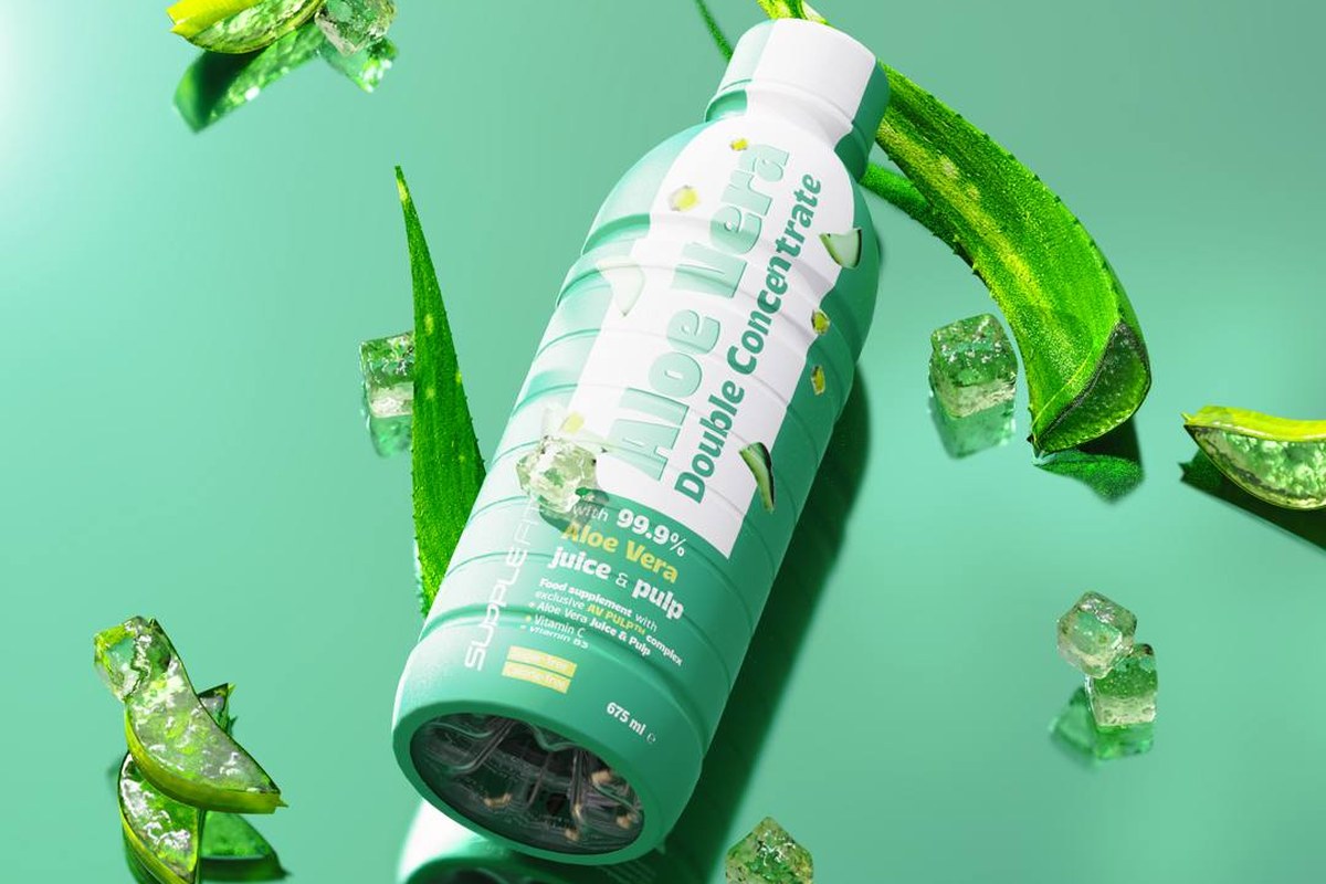 A bottle of aloe vera juice and pulp surrounded by fresh aloe leaves and ice on a green background