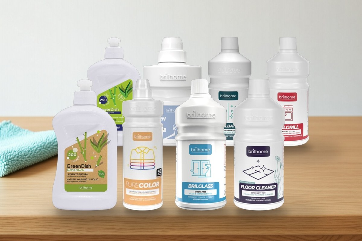 Eight Brilhome cleaning bottles standing on a light oak table beside a folded turquoise microfibre cloth