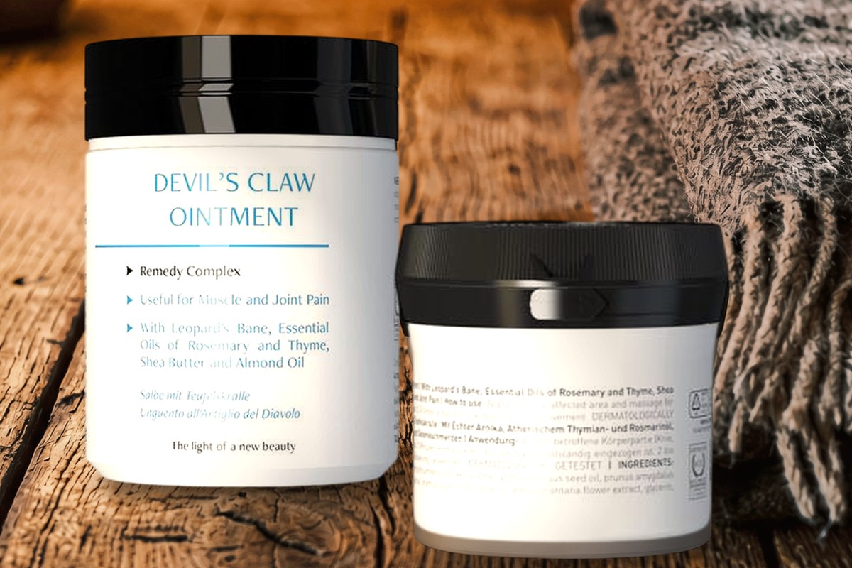 Two jars of Devil's Claw Ointment, 150 ml and 50 ml, on an old oak table in warm lamplight, a folded grey wool blanket beside them